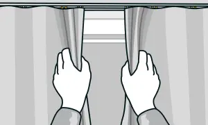 Två händer drar isär grå gardiner som hänger i en gardinskena i taket.