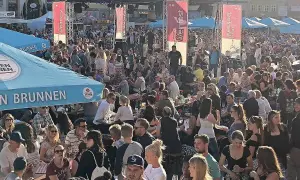 Menschenmenge feiert beim Bamberger Weinfest. Eine Bühne mit Musikern, Fahnen und Zelten. Viele Besucher sitzen an Tischen, trinken und genießen die Atmosphäre.