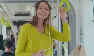 Uśmiechnięta dziewczyna w słuchawkach słucha podcastów po angielsku w tramwaju, trzymając się poręczy.