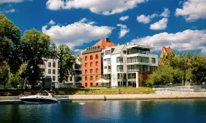 Nowoczesne budynki nad wodą, przypominające hotel Almond, z łodzią przy nabrzeżu i błękitnym niebem.