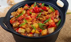 Un plat de ratatouille colorée, avec des morceaux d'aubergine, de courgette, de poivron rouge et de tomate, garni de ciboule fraîche. Une recette savoureuse.