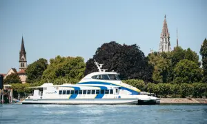 Schnelles Katamaran-Schiff auf dem Bodensee, mit Kirchtürmen von Friedrichshafen und Konstanz im Hintergrund.