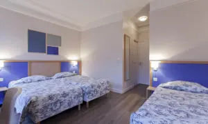 Pokój hotelowy z trzema łóżkami w niebiesko-białą pościelą i niebieskimi zagłówkami.