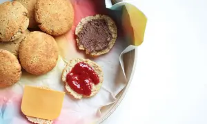 Scones med keso, chokladpålägg och sylt på en bricka. En skiva ost ligger på en scone.