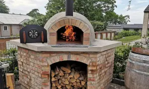 En vacker, murad pizzaugn med eld som sprakar i öppningen. Ved ligger staplad under ugnen, redo för nästa pizzakväll.