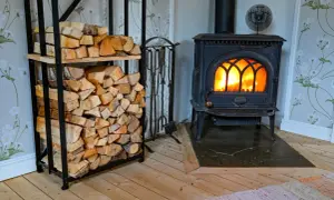 En mysig brasa sprakar i en gjutjärnskamin. Bredvid står en hylla fylld med ved, redo att installera braskamin för värme och trivsel.