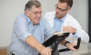 Un homme âgé sourit en effectuant un **test d'effort vélo**, supervisé par un médecin en blouse blanche.