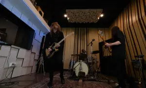 Zakk Cervini and his band rock out in a studio, with a guitarist in the foreground, a bassist to the right, and a drummer in the background.
