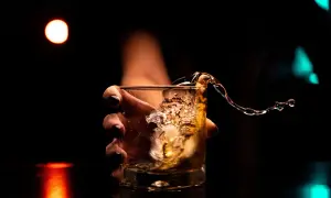 Dłoń trzyma szklankę z whisky, gdy płyn rozlewa się, tworząc falę. Kto wydaje koncesję na alkohol, by móc cieszyć się takimi chwilami?