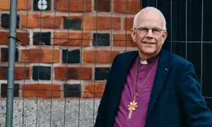 Biskop Marianne Langby Modéus ler mot kameran, klädd i en lila skjorta och en mörk kavaj. En guldkorshalsband hänger över hennes bröst.