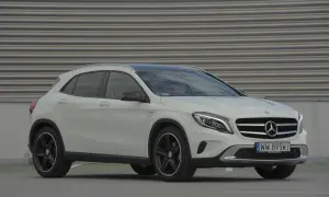 Biały Mercedes GLA na tle szarej, falistej ściany. Zbliżenie na przód auta, widoczne logo i tablica rejestracyjna. Idealny do miasta, poznaj jego mercedes gla wymiary.