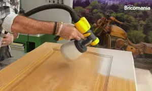 Hombre pintando una puerta de madera con una pistola pulverizadora. El resultado es un acabado liso y uniforme.