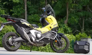 Żółty Honda X-ADV 750 z czarnymi akcentami, gotowy na przygodę. Obok bagażnik kufer.