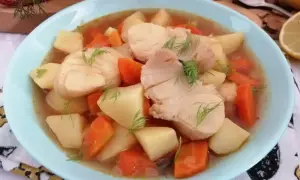 Miska zupy rybnej z kawałkami ryby, ziemniaków i marchewki, udekorowana koperkiem.