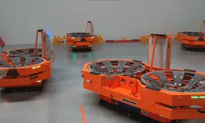 Pomarańczowy robot mobilny z numerem 22 w magazynie. W tle inne roboty i regały.
