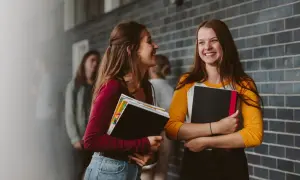 Dwie uśmiechnięte uczennice z książkami rozmawiają o systemie rekrutacji do szkół ponadpodstawowych.