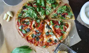 Pizza podzielona na pół: jedna połowa z pesto i rukolą, druga z sosem pomidorowym i bazylią.