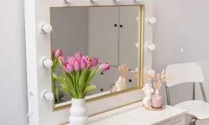 Eleganckie lustro makijażowe z żarówkami, ozdobione bukietem różowych tulipanów i świecami. Idealne do porannego rytuału.