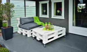 Sofá y mesa de centro hechos con pintura para palets, con cojines grises y manta verde.