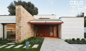 Casa moderna con acabados de fachadas de piedra y paneles blancos. Un camino de baldosas conduce a la entrada principal de madera.