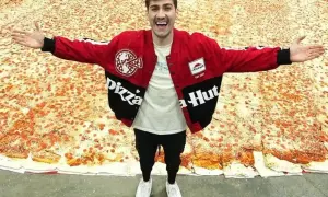 Mężczyzna w kurtce Pizza Hut stoi na gigantycznej pizzy.