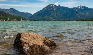 Kitesurfer tanzen über das Wasser am Bad Wiessee, während Segelboote und Berge im Hintergrund ruhen.