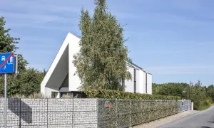 Nowoczesny dom z białej bryły, otoczony gabionowym ogrodzeniem. W tle drzewa i błękitne niebo. To idealny plot akustyczny.