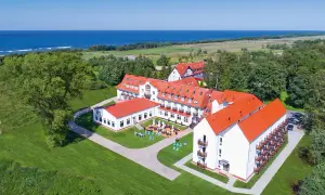 Hotel Mona Lisa Kołobrzeg z widokiem na morze. Białe budynki z czerwonymi dachami otoczone zielenią.