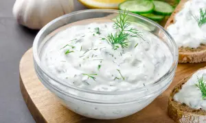 Un bol de salsa de yogur con eneldo y pepino, listo para untar en pan tostado.