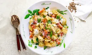 Pyszne tortellini z boczkiem i śmietanowym sosem, idealne jako pomysł na obiad. Posypane natką pietruszki.