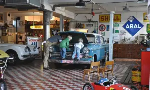 Familie inspiziert blauen Oldtimer in Werkstatt. Die Restaurierung des Autos scheint ein gemeinsames Projekt zu sein.