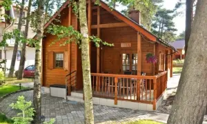 Drewniany domek z werandą i stolikiem, otoczony drzewami. Idealne miejsce na wypoczynek przez cztery pory roku w Dźwirzynie.