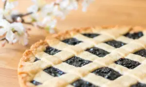 Ein köstliches Crostata-Rezept mit Blaubeerfüllung und Gittermuster, daneben zarte weiße Blüten.