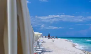 File di ombrelloni bianchi aprono la vista sulla spiaggia di Marotta, con lettini pronti e il mare turchese sotto un cielo azzurro.