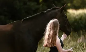 Dziewczyna głaszcze ciemnego konia. Czas ruje u klaczy jest zmienny, ale ta chwila jest spokojna.