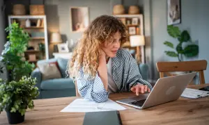 Donna con capelli ricci lavora al computer, documenti sul tavolo. Forse sta cercando informazioni su un mutuo con garante genitore per realizzare un sogno.