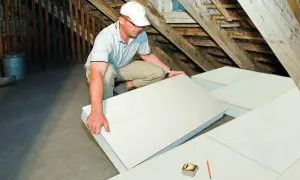 Operaio posa pannelli per isolamento termico in sottotetto. Materiali isolanti edilizia per un tetto efficiente.