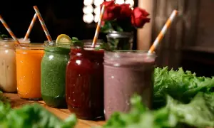Fem färgglada smoothies i glasburkar, redo för en bebis att njuta av. Grönt, orange, rött och lila.