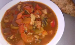 Pyszne leczo z pieczarkami, papryką i kurczakiem w sosie pomidorowym, podane z chlebem.
