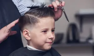 Chłopiec w salonie fryzjerskim, gdzie powstają modne fryzury dla chłopców 8 lat. Fryzjerka modeluje jego włosy.