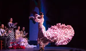 Bailarina de flamenco con un vestido de lunares rojos y blancos, su falda ondea con gracia. El público aplaude la seguidilla flamenca.