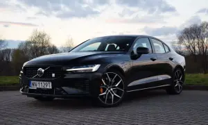 Czarny Volvo S60 T8 na tle zachodzącego słońca i drzew. Elegancki sedan z charakterystycznym grillem i felgami.