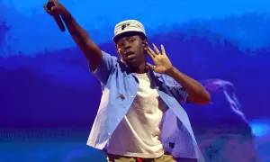 Tyler The Creator w Krakowie, w niebieskiej koszuli i czapce, z mikrofonem w dłoni.