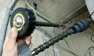 Domowy sposób na czyszczenie instalacji: ręka trzyma narzędzie z okrągłą głowicą, podłączone do elastycznego węża, który prowadzi do rur.