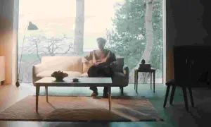 En person sitter i en soffa i ett rum med dansk design inredning. Ett stort fönster visar en vinterskog.