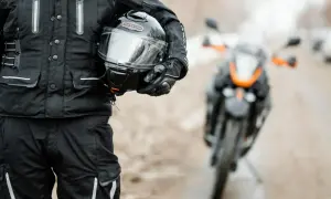 Motocyklista w czarnym ubraniu, trzymający kask. Gotowy na jazdę skuterem 125.