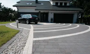 Nowoczesny podjazd z kostki brukowej i żwiru, z eleganckim lany beton na podjazd. Czarny samochód parkuje przed domem.