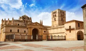 Imponente catedral románica en España, con su torre campanario y cúpula, bajo un cielo azul con nubes.