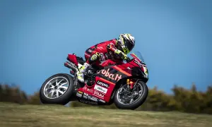 Piloto de SBK hoy en acción, con su moto Ducati roja y negra, inclinándose en una curva.