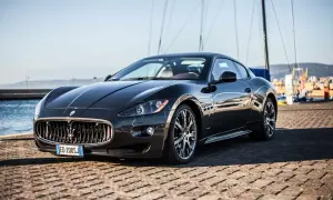 Elegancki, czarny Maserati coupe lśni w słońcu na tle portu z żaglówkami.